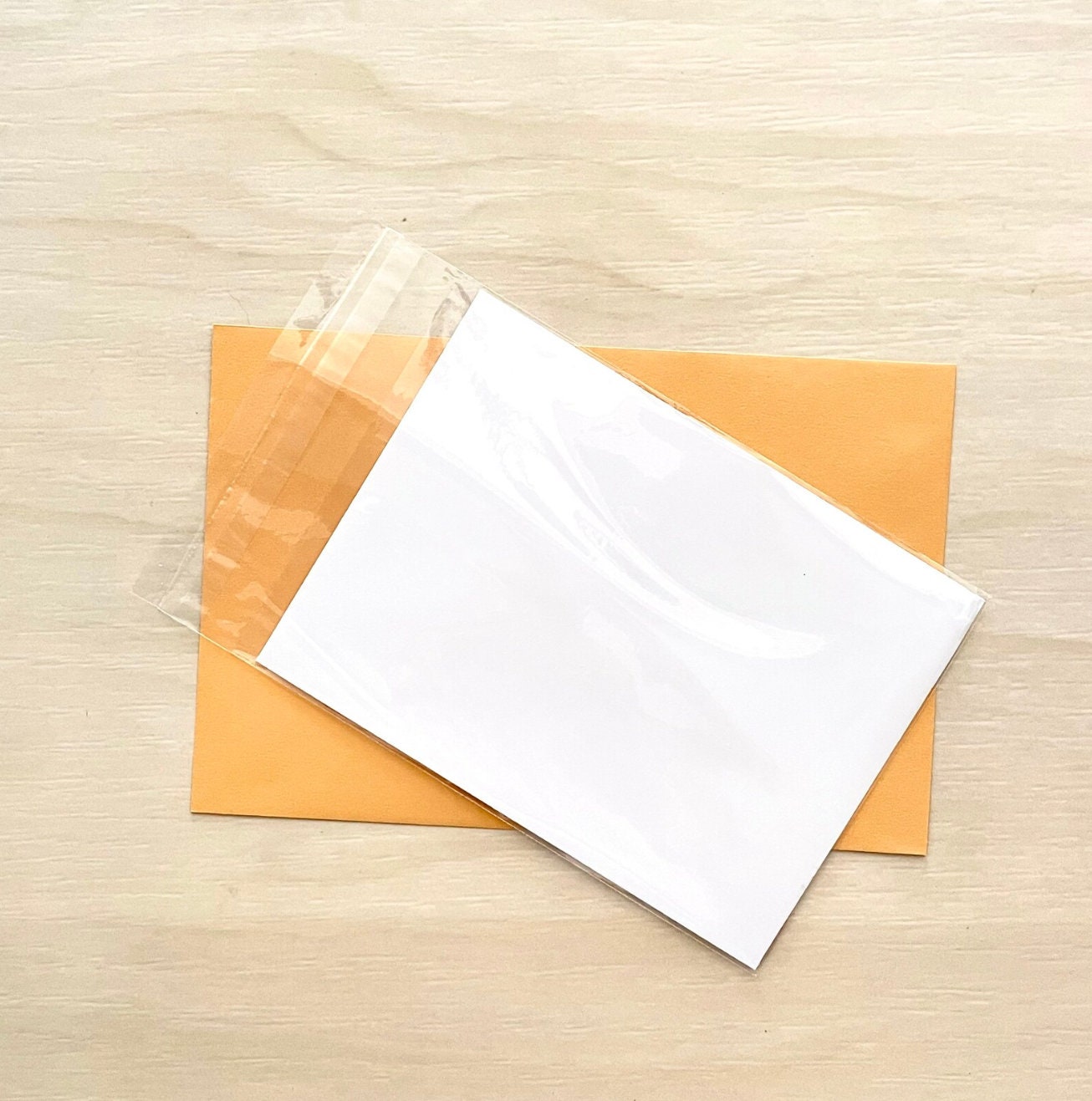 White envelope on an orange envelope with clear plastic wrap on a wooden surface