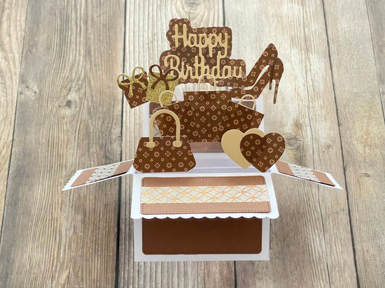 Pop-up birthday card with high heels, cake, and 'Happy Birthday' on a wooden surface