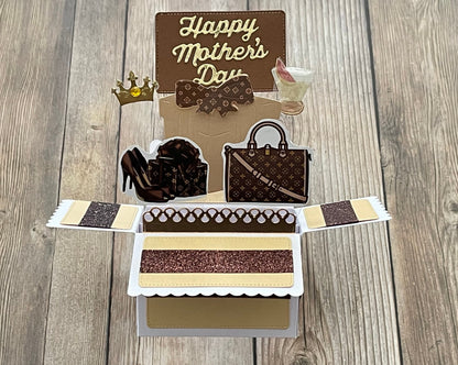 Card with 'Happy Mother's Day' text, high heels, handbag, and tiara on a wooden surface
