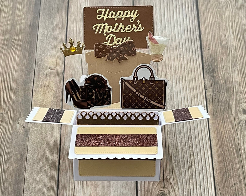 Card with 'Happy Mother's Day' text, high heels, handbag, and tiara on a wooden surface