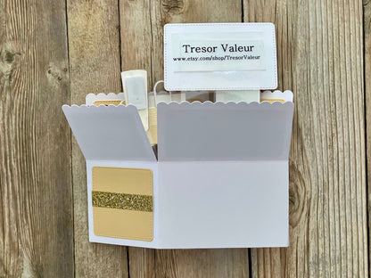 Open white cardholder with gold card and Tresor Valeur branded card on a wooden surface