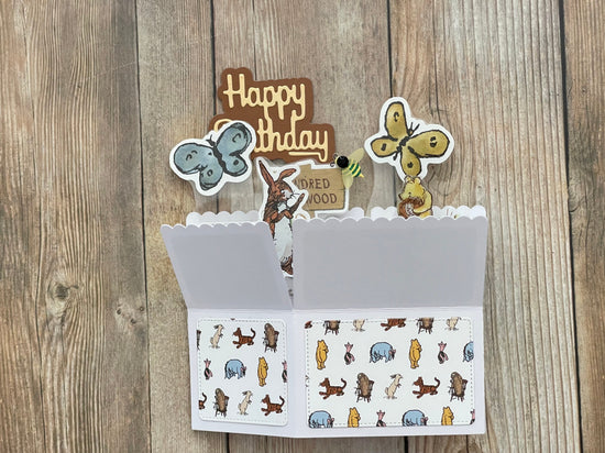 Open card with birthday decorations and illustrations on a wooden surface