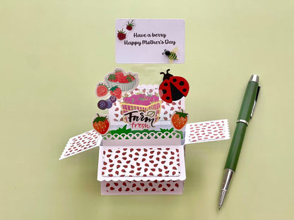 Open card with ladybug and strawberry design, pen on a light green background