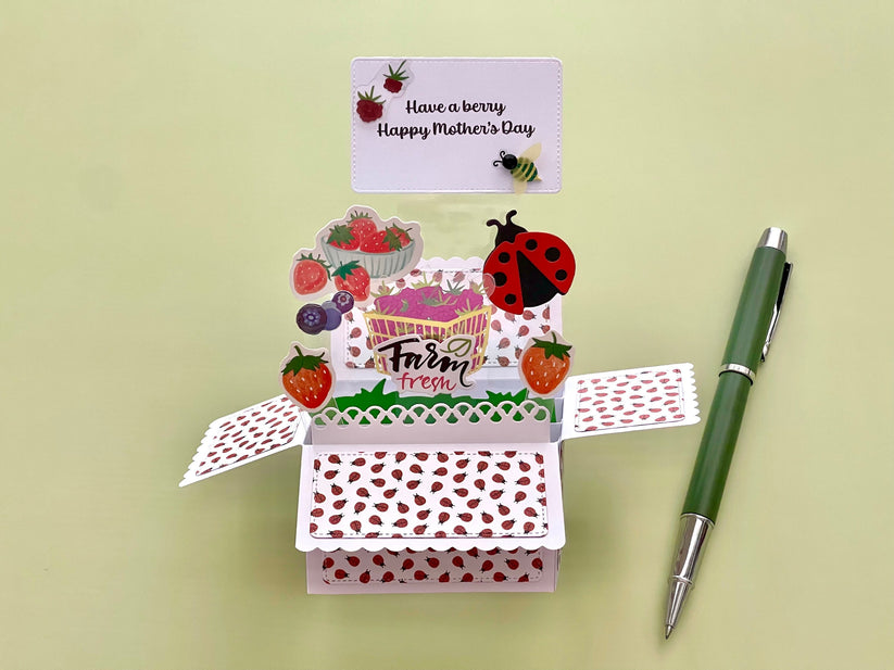 Open card with ladybug and strawberry design, pen on a light green background