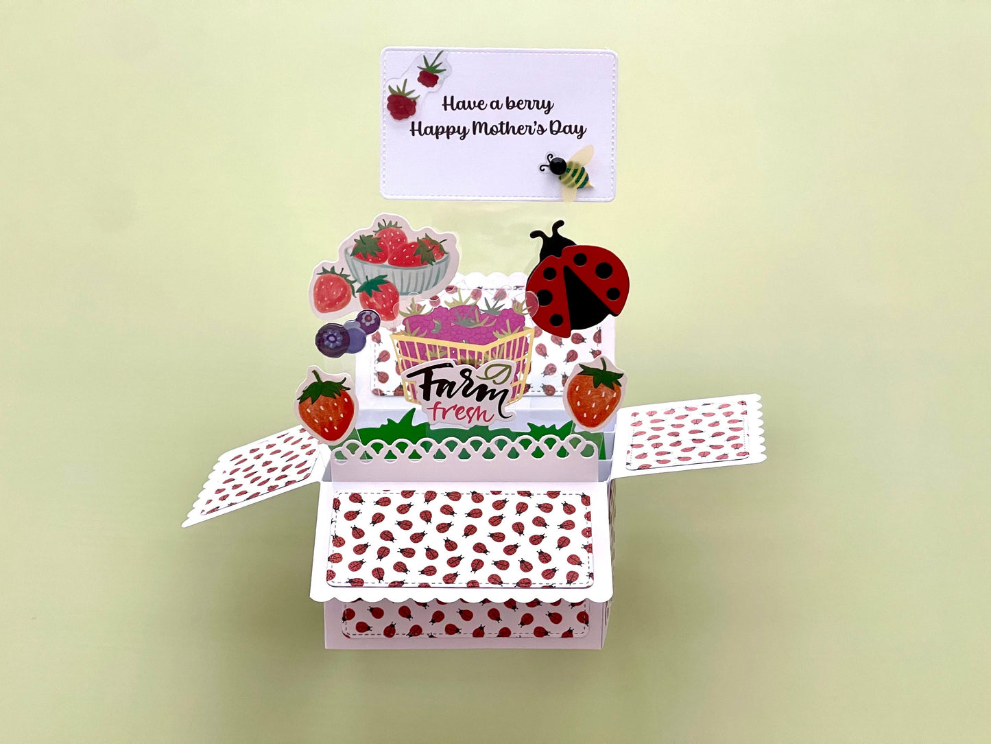 Mother's Day pop-up card with a ladybug and strawberry design on a light green background