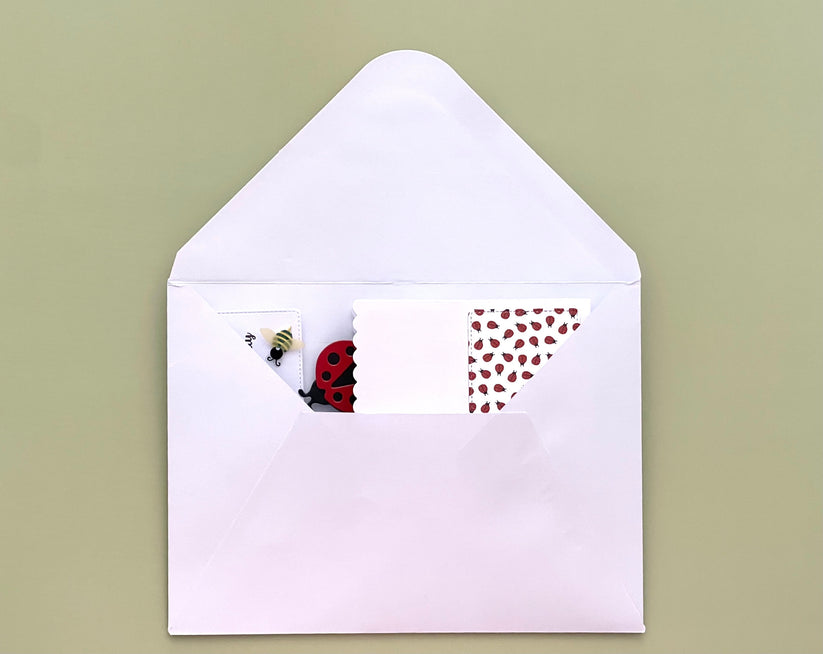 White envelope with a card featuring a ladybug design on a green background