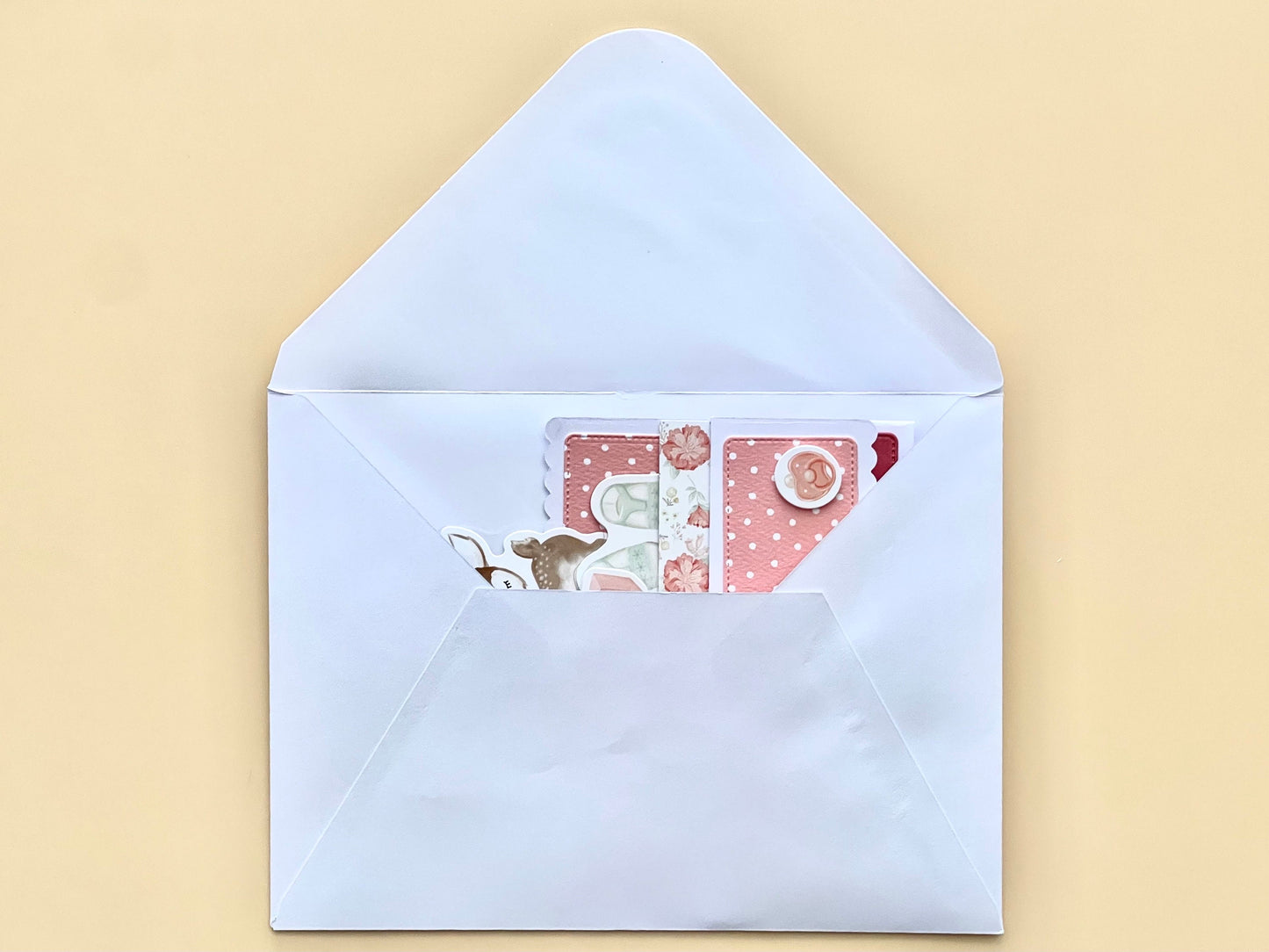 Open light blue envelope with a pink card featuring a cartoon character on a beige background