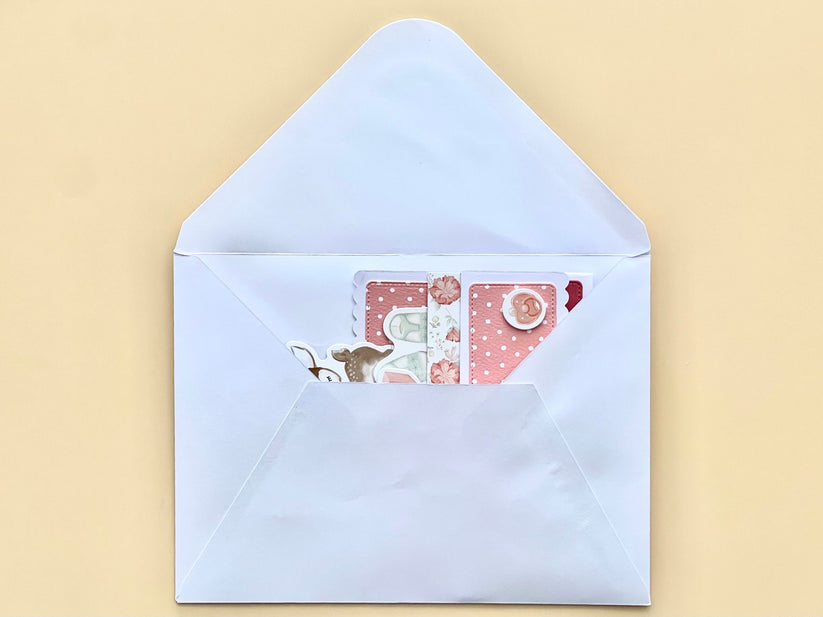 Open light blue envelope with a pink card featuring a cartoon character on a beige background