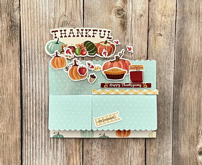 Thanksgiving-themed card with pumpkins, pies, and other fall elements on a wooden background.