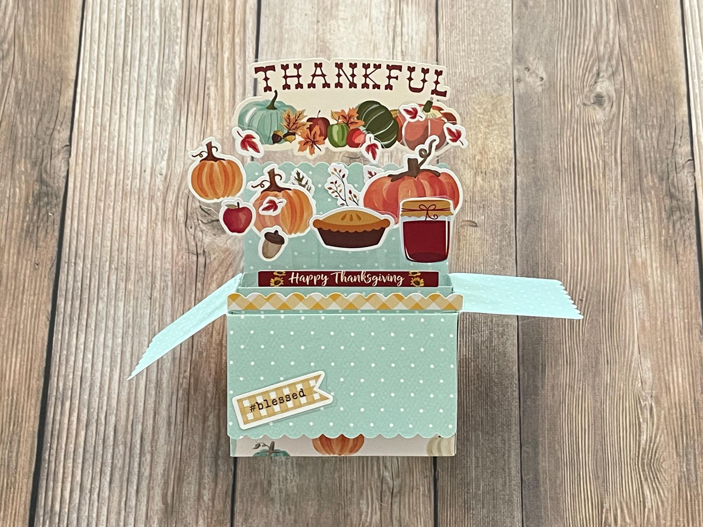 Thanksgiving-themed pop-up card with pumpkins, pies, and other fall elements on a wooden surface.