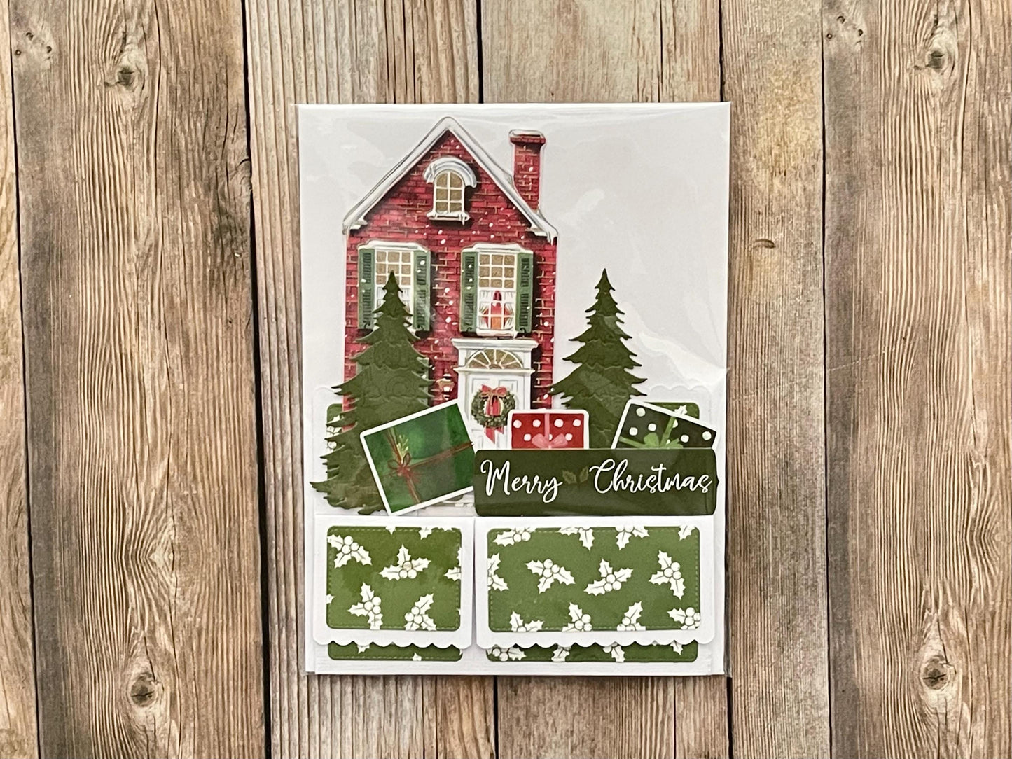 Christmas-themed card with a house and trees on a wooden surface