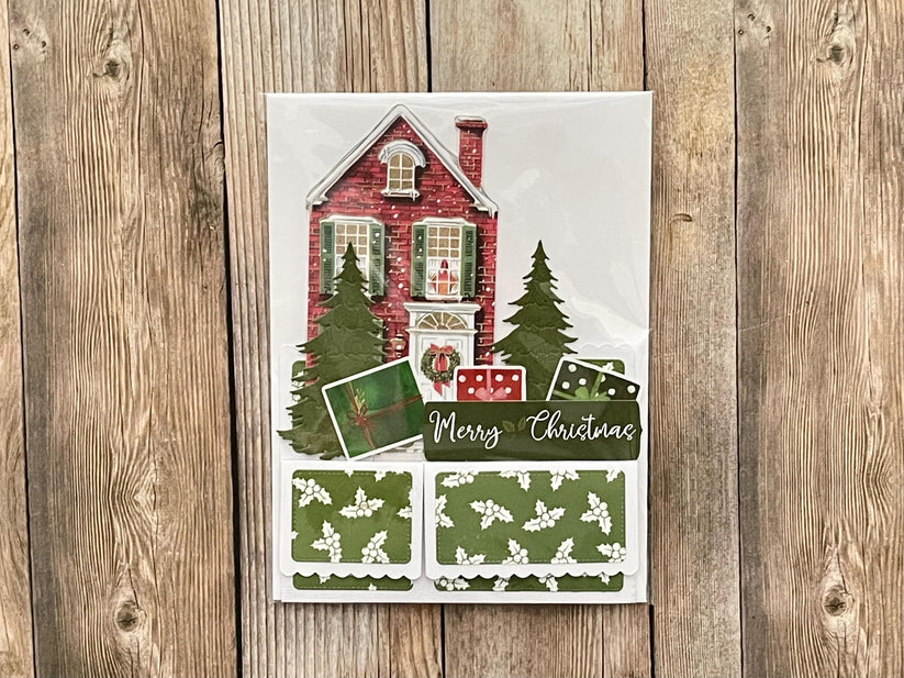 Christmas-themed card with a house and trees on a wooden surface