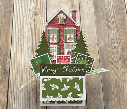 Christmas-themed card with a house and trees on a wooden surface
