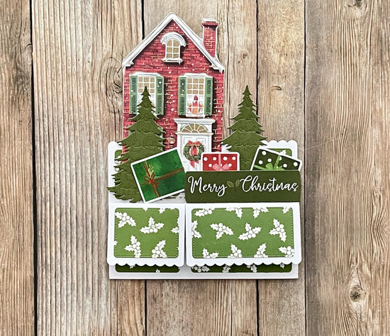 Christmas-themed card with a house, trees, and gift boxes on a wooden background