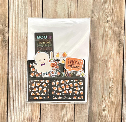 Halloween-themed card with candy corn pattern and ghost illustration on a wooden surface