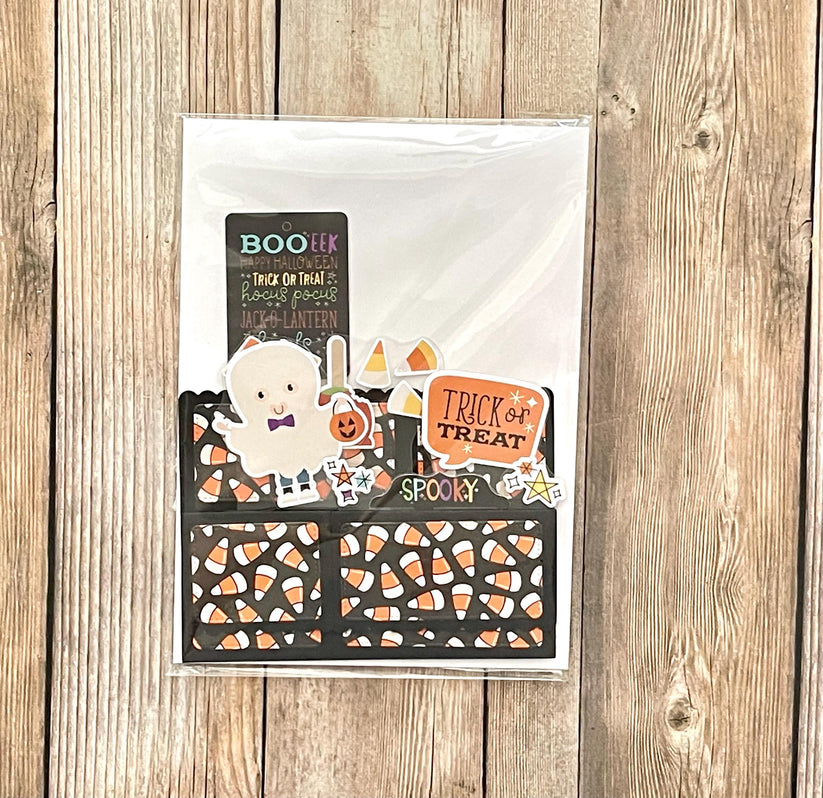 Halloween-themed card with candy corn pattern and ghost illustration on a wooden surface