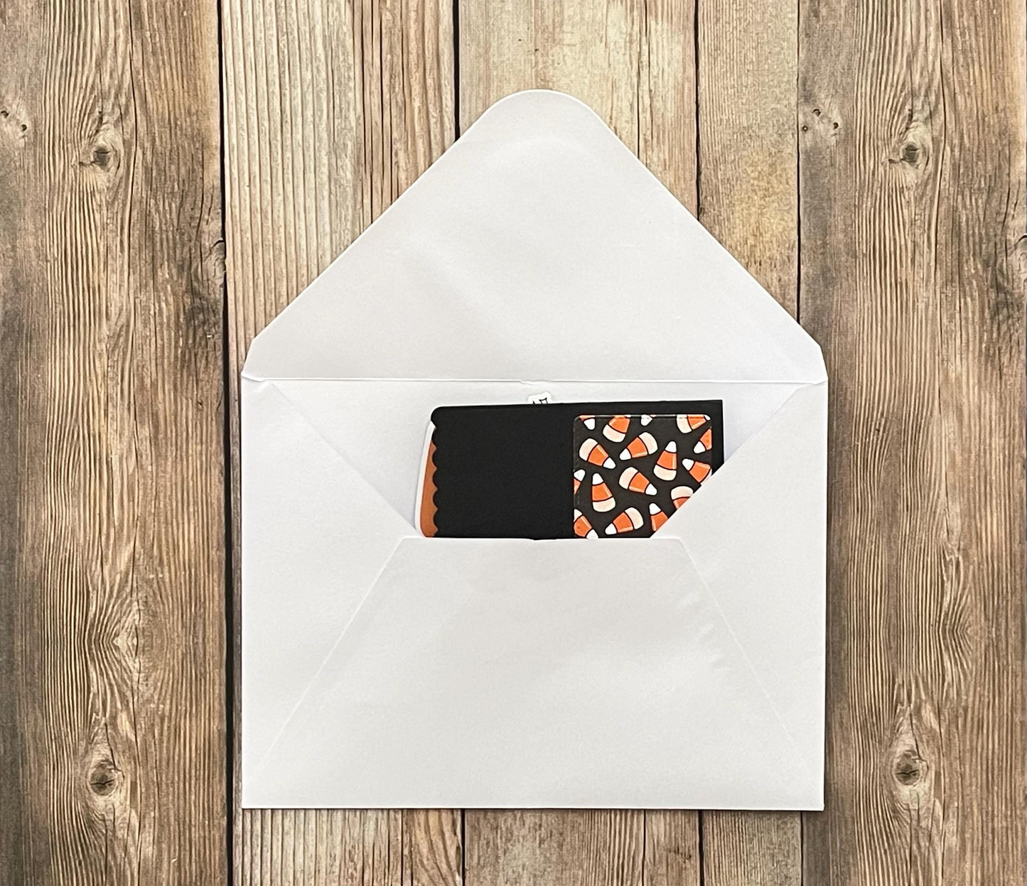 Black card with candy corn pattern inside a white envelope on a wooden surface
