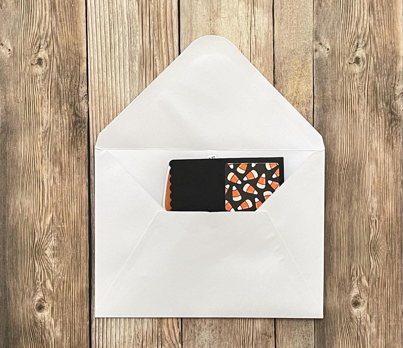 Black card with candy corn pattern inside a white envelope on a wooden surface