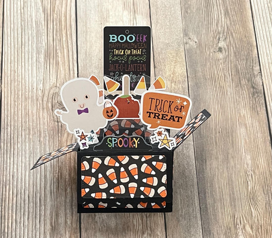 Halloween-themed decorative box with ghost, pumpkin, and candy corn design on a wooden surface.