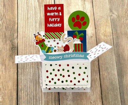 Christmas-themed card with cat illustrations and text on a wooden surface