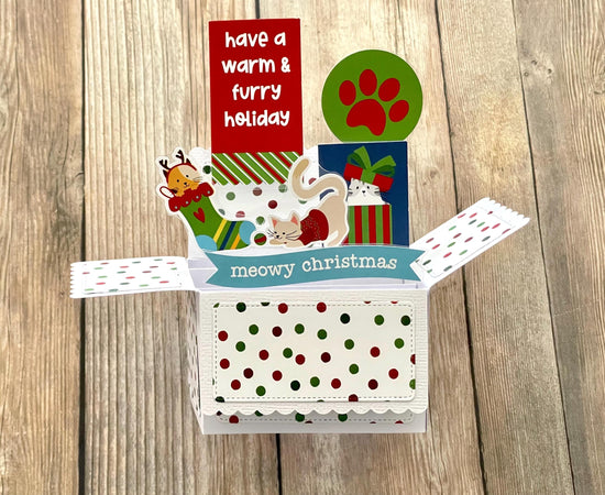 Christmas-themed card with cat illustrations and text on a wooden surface