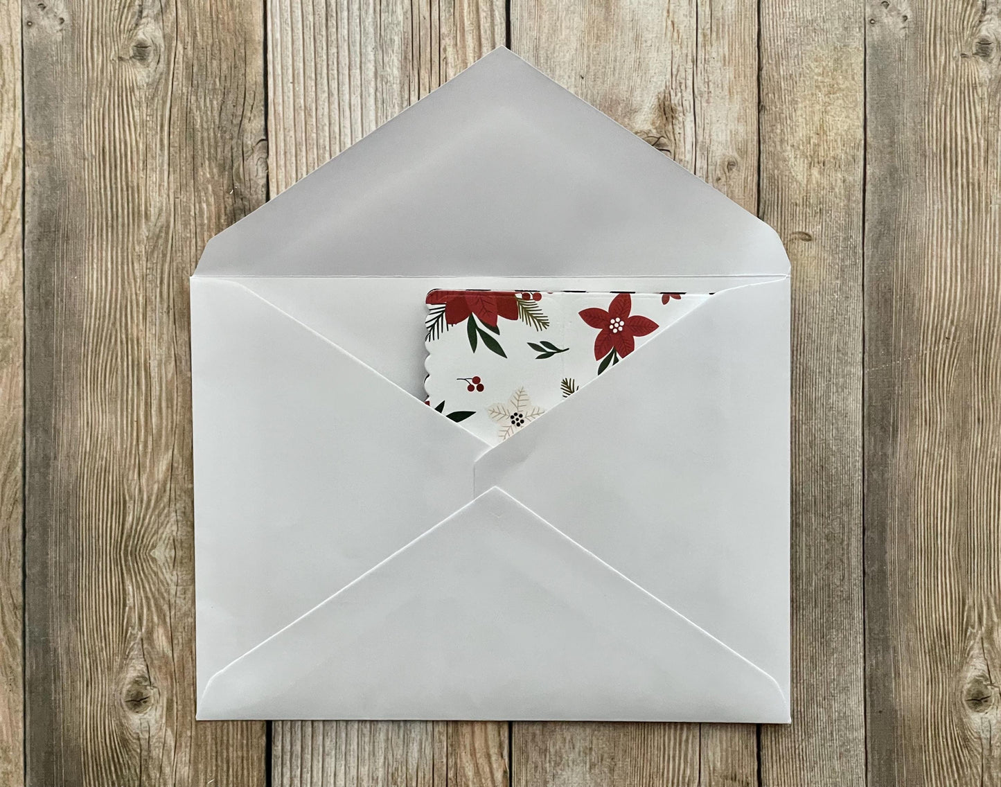 Open white envelope with floral card on a wooden surface