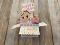 Pop-up birthday card with pigs, a house, and a duck on a wooden surface
