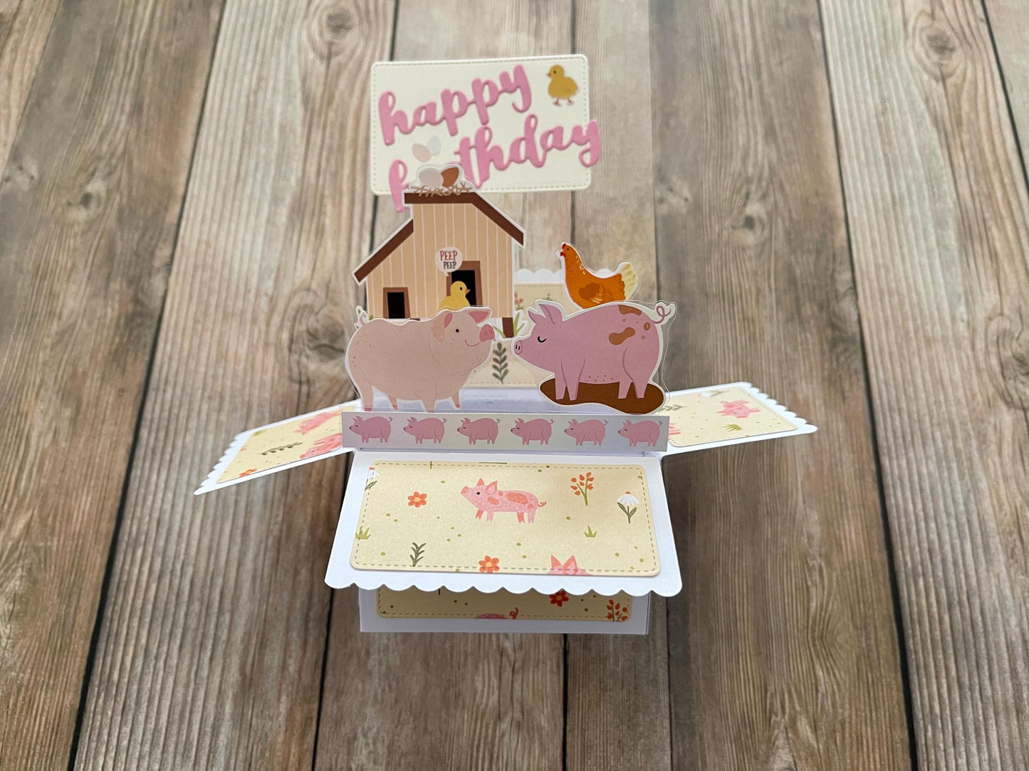 Pop-up birthday card with pigs, a house, and a duck on a wooden surface