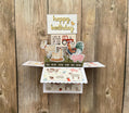 Pop-up birthday card with farm animal illustrations on a wooden background