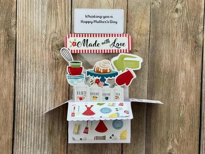 Pop-up  Mother's Day card with a baking theme, 'Made with Love' message and "Whisking you a Happy Mother's Day" on a wooden background