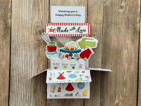 Pop-up  Mother's Day card with a baking theme, 'Made with Love' message and "Whisking you a Happy Mother's Day" on a wooden background