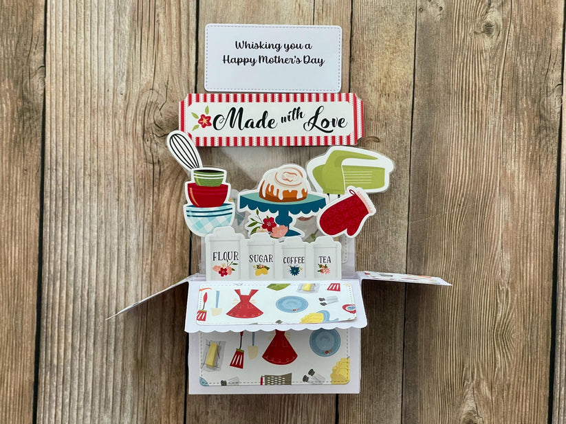Pop-up  Mother's Day card with a baking theme, 'Made with Love' message and "Whisking you a Happy Mother's Day" on a wooden background